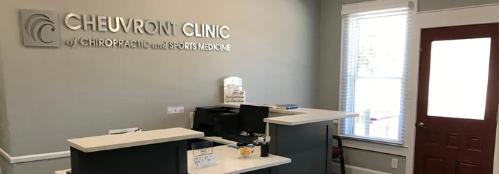 Clinic reception area with a dark front desk, computer, window, entrance door, and wall signage.